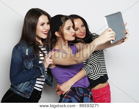 Three girls friends taking selfie with digital tablet, studio shot over gray vackground
