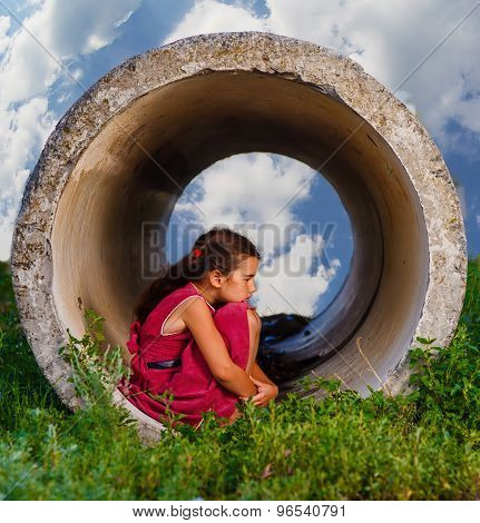 Homeless teenager girl sits on his haunches in the concrete pipe