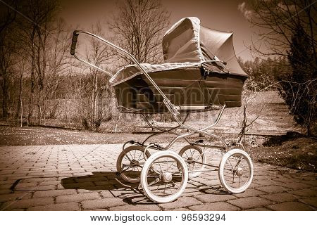 Retro style baby carriage outdoors on sunny day, sepia filter