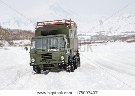 KAMCHATKA PENINSULA RUSSIA - APRIL 4 2014: Old Swedish military off-road vehicle Volvo Laplander C304 (six-wheel drive) khaki color driving in snow along a country road on background volcanoes.