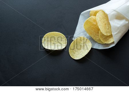 Potato chips in a paper bag on black background