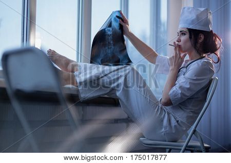 Brunette sassy female nurse in uniform smoking a cigarette and looking at x-ray picture of backbone