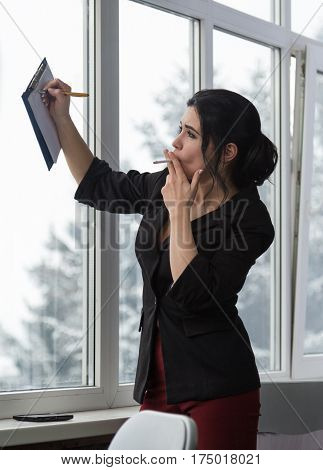 Business woman in office with a cigarette makes notes in notepad