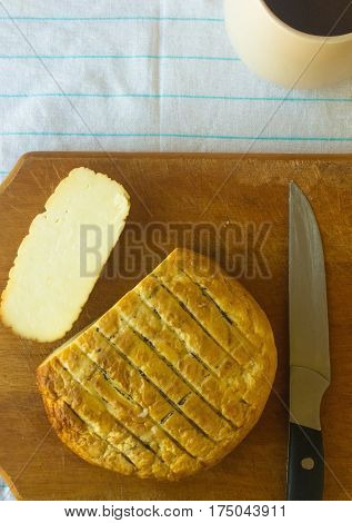 cut head of traditional Adygei cheese handmade with knife and a Cup of coffee on wooden Board