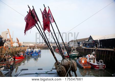 WHITSTABLE, UK -February 24, 2017: Fishing Boats in Whitstable Harbour in portrait view with warehouse in background