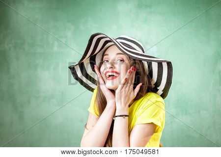 Colorful portrait of a beautiful woman in yellow t-shirt and striped hat on the green background