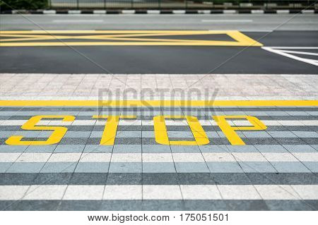 Roadway and pave with the yellow and white road marking on them. There are dividing lines and a Stop inscription. Closeup. Horizontal.