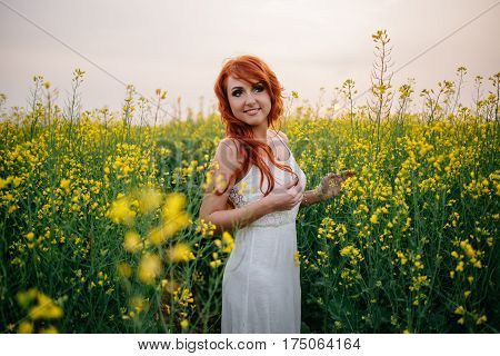 Young beautiful red-haired woman in a blooming rapeseed field at sunset