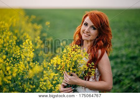Young beautiful red-haired woman in a blooming rapeseed field at sunset