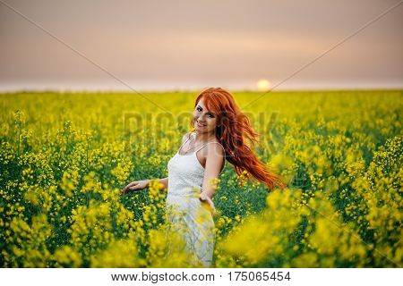 Young beautiful red-haired woman in a blooming rapeseed field at sunset