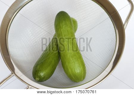 Two green cucumbers in a kitchen sieve.