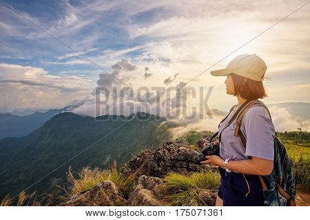 Hiker asian young woman happy with camera backpack and caps looking beautiful landscape nature of mountain and colourful sky at sunset on viewpoint Phu Chi Fa Forest Park Chiang Rai Thailand