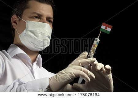 Young Man As A Doctor Gives A Medical Injection To Nigerien Flag On A Black Background