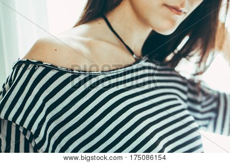 Closeup portrait of Caucasian young beautiful woman model with messy long hair in striped t-shirt by window indoor showing one bare shoulder toned with filters