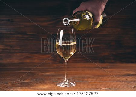 Pouring white wine from a bottle in a close up view of the wineglasses against wooden background