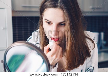Closeup portrait of young beautiful Caucasian white girl woman doing her makeup applying lipstick in front of the mirror in morning at home candid lifestyle natural light toned with filters