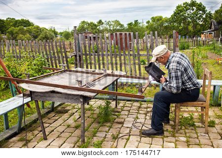 Aged man welding metal structure at his dacha