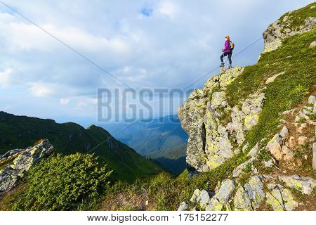 Sporty girl with back sack is standing at the edge of the precipice and watching on the endless vast of mountains landscape in the sunny day.
