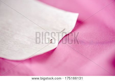 needlework and tailoring concept - paper pattern attached with sewing pin to cloth