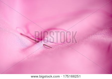 needlework and tailoring concept - sewing needle with thread stuck into pink fabric