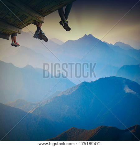 Group of hikers sit on a wooden flooring above the mountain valley and enjoy majestic sunset.