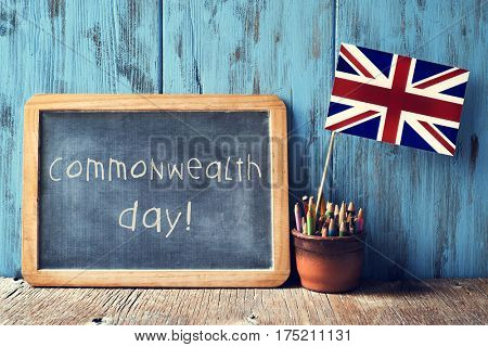 a wooden-framed chalkboard with the text commonwealth day written in it and the Union Flag in a pot of pencils, against a blue rustic wooden background
