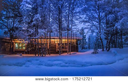 Romantic view of old traditional wooden forest cabin in the woods embedded in scenic northern winter wonderland scenery in beautiful mystic twilight during blue hour at dusk