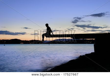 Un giovane seduto su un molo al tramonto, presso il fiordo di Oslo, Norvegia
