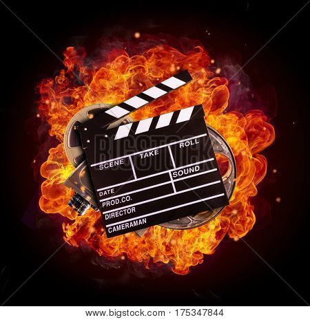 Film clapper, reel and camera in fire, isolated on black background. Concept of filmmaking.