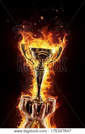 Man hands holding burning gold trophy cup as a winner, flames around. Concept of success and effort. Isolated on black background