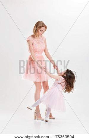 blonde mom and sweet little daughter in pink dresses princesses hugging and laughing on gray background. family