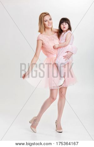 mom blonde holding a cute little daughter in a pink Princess dress on a gray background. family