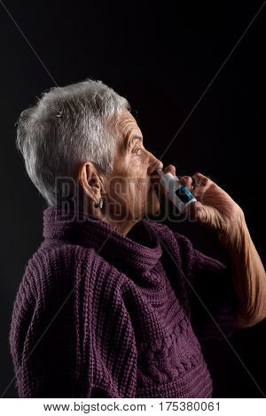 Old woman with nasal spray on a black background