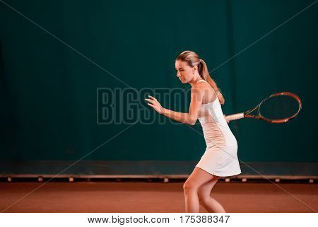Indoor tennis court playing athlete. Young woman playing tennis
