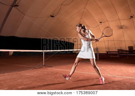 Sportswoman at the tennis court with racquet. Indoor tennis court
