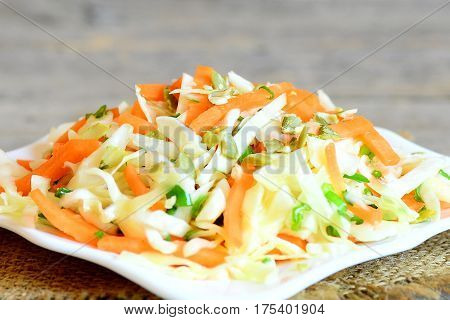Easy homemade coleslaw salad. Tasty coleslaw salad with carrots, green onion and pumpkin seeds on a plate and on a wooden table. Fresh vegetable meal. Closeup