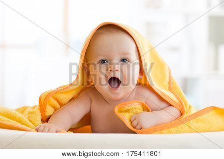 Smiling baby covered soft towel. Cute child lying on bed after bathing or shower in living room