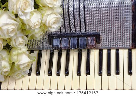 Vintage accordion and a bouquet of white roses. Concept of a nostalgic music. Still life with a traditional folk musical instrument.