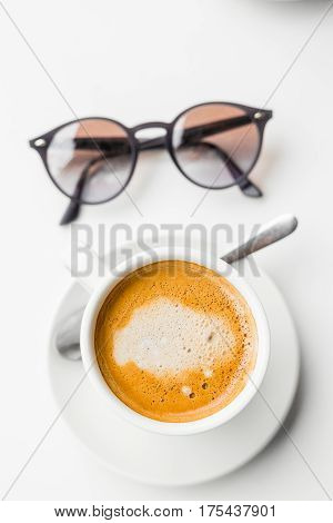 Closeup hipster eyeglasses and cup of cappuccino on the white table