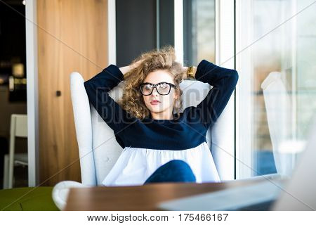Business woman relaxing working at office desk laid back resting on chair with hands behind head. Work satisfaction businesswoman taking break after goal success or enjoying her job achievement.