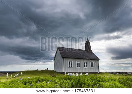 Strandkirkja on Iceland with Icelandic flag green meadow graveyard and dark rain clouds.