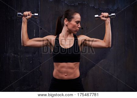 Close-up of muscular female doing biceps curl with dumbbells. Strength workout of muscular confident female doing biceps curl with dumbbells. Showing her pumped biceps, triceps and press