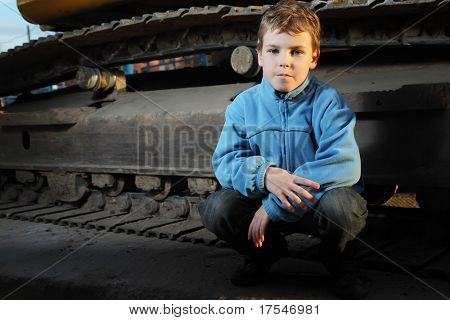 Little boy in giacca blu seduto vicino a trattore cingolato nel buio