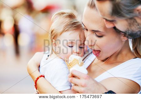 A baby boy is being hugged by his mother and father while fed with ice cream.
