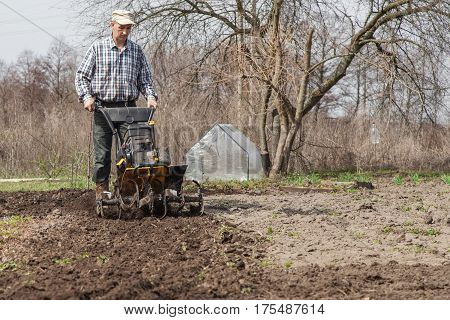 Man working in the garden with garden tiller. Garden tiller to work. Man with tractor cultivating field at spring. Farmer loosens soil by petrol cultivator