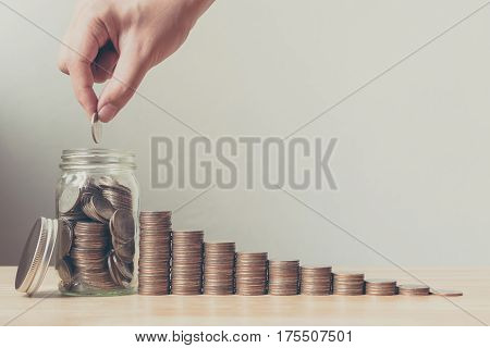 Hand of male or female putting coins in jar with money stack step growing growth saving money Concept finance business investment