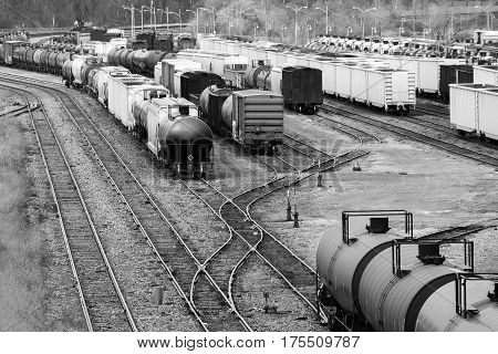 Many boxcars and cargo shipping train cars on tracks in a busy trainyard in black and white