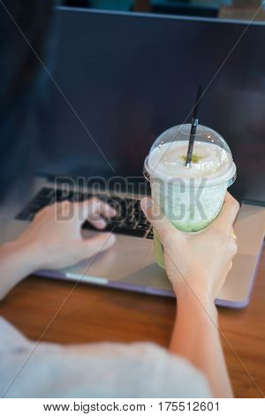 Woman Hand On Iced Milk Green Tea During Typing stock photo