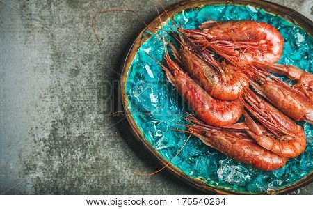 Raw uncooked red shrimps on chipped ice in turquoise blue ceramic tray over grey concrete background, top view, copy space, horizontal composition. Fresh seafood concept