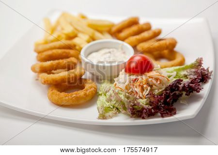 Battered Onion Rings And French Fries With Sauce On A White Plate